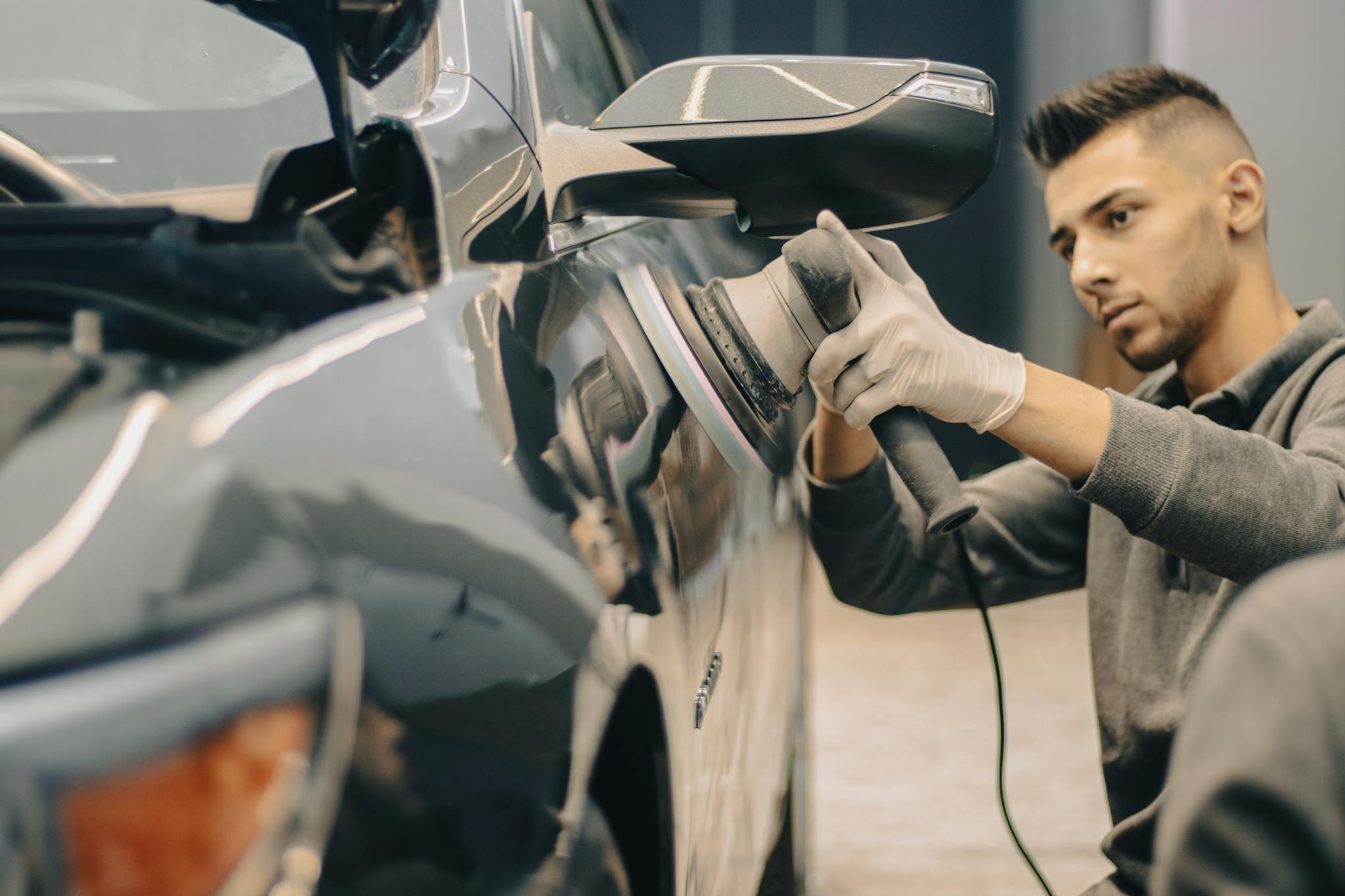 A focused worker polishes a vehicle with precision, enhancing its shine indoors.